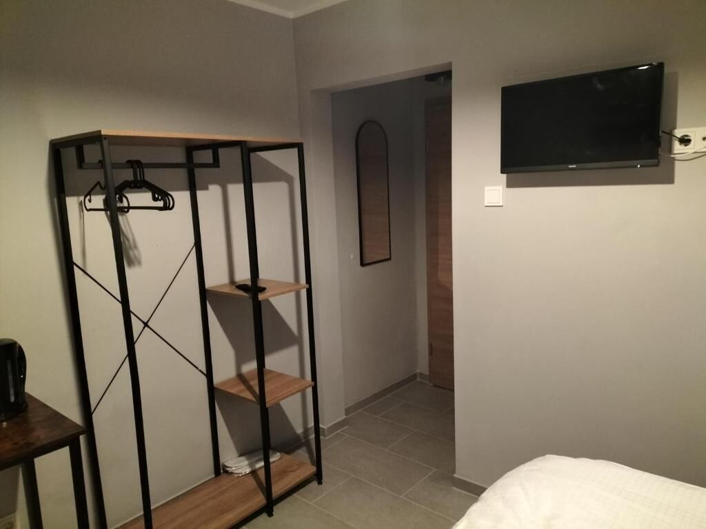 A bedroom with a bed, a TV mounted on the wall, a wardrobe with shelves, and a door leading to another room.