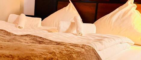 A neatly made bed with white linens and a brown throw blanket, a dark headboard, and a wall-mounted light switch.