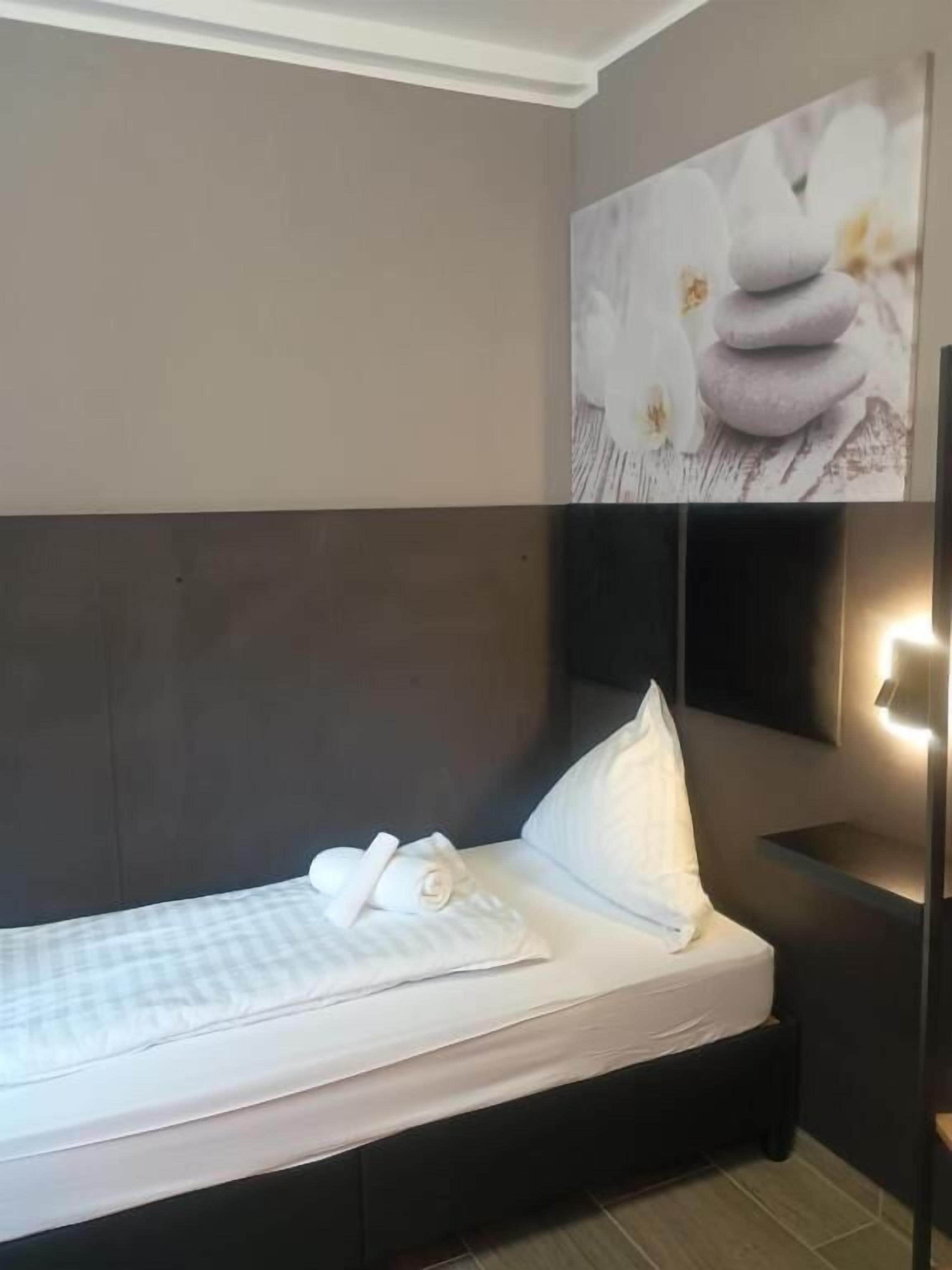 Een opgemaakt bed met witte lakens en kussens, een hoofdbord en een aan de muur bevestigde lamp.