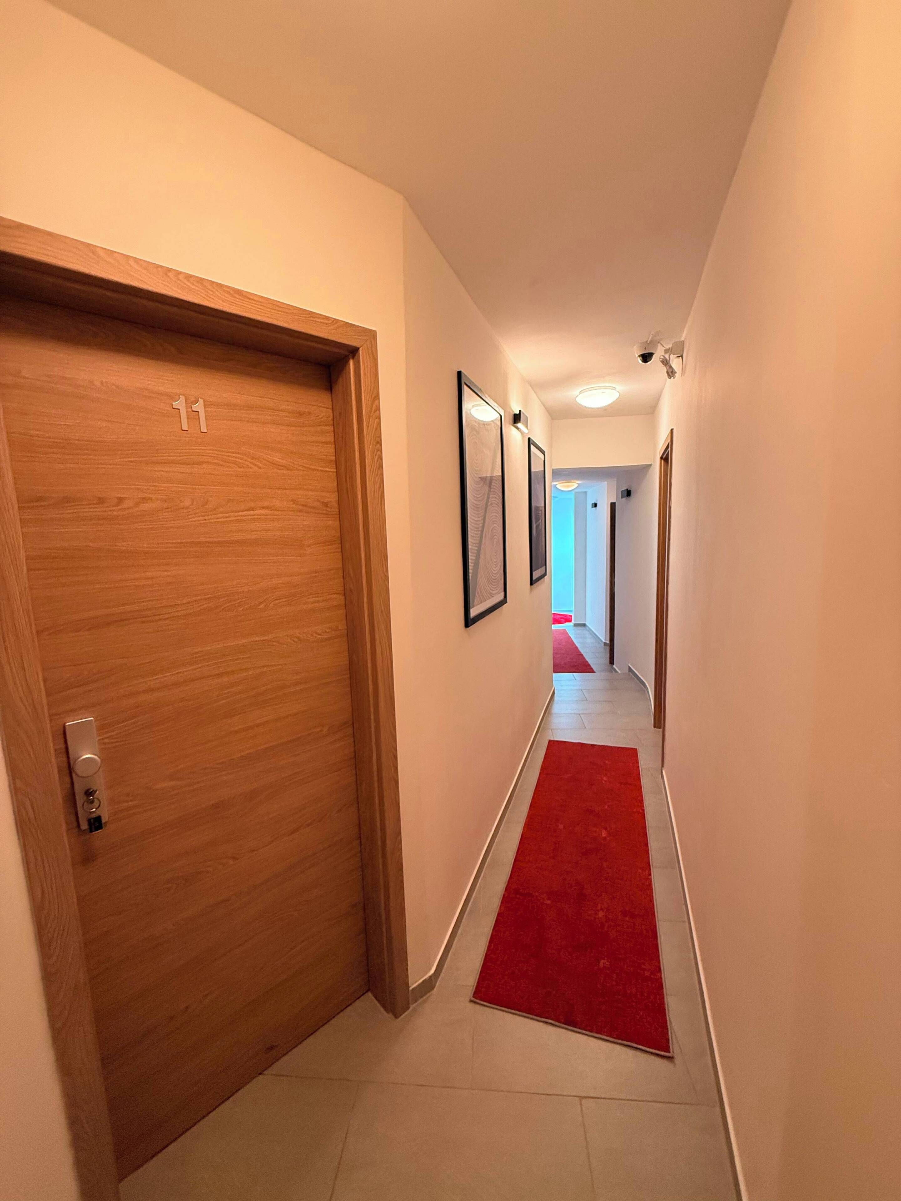 A hotel hallway with a wooden door marked '11', a red carpet, and framed artwork on the walls.