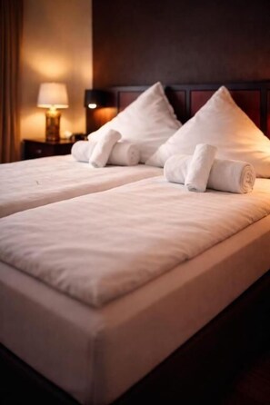 A hotel room with two beds, each with a neatly folded white towel, a lamp on a bedside table, and a dark headboard. - Niehler Hotel (Cologne)