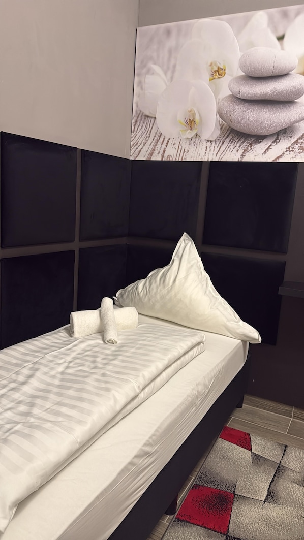 A bed with white bedding, a pillow, and a headboard with a textured design. - Niehler Hotel (Cologne)