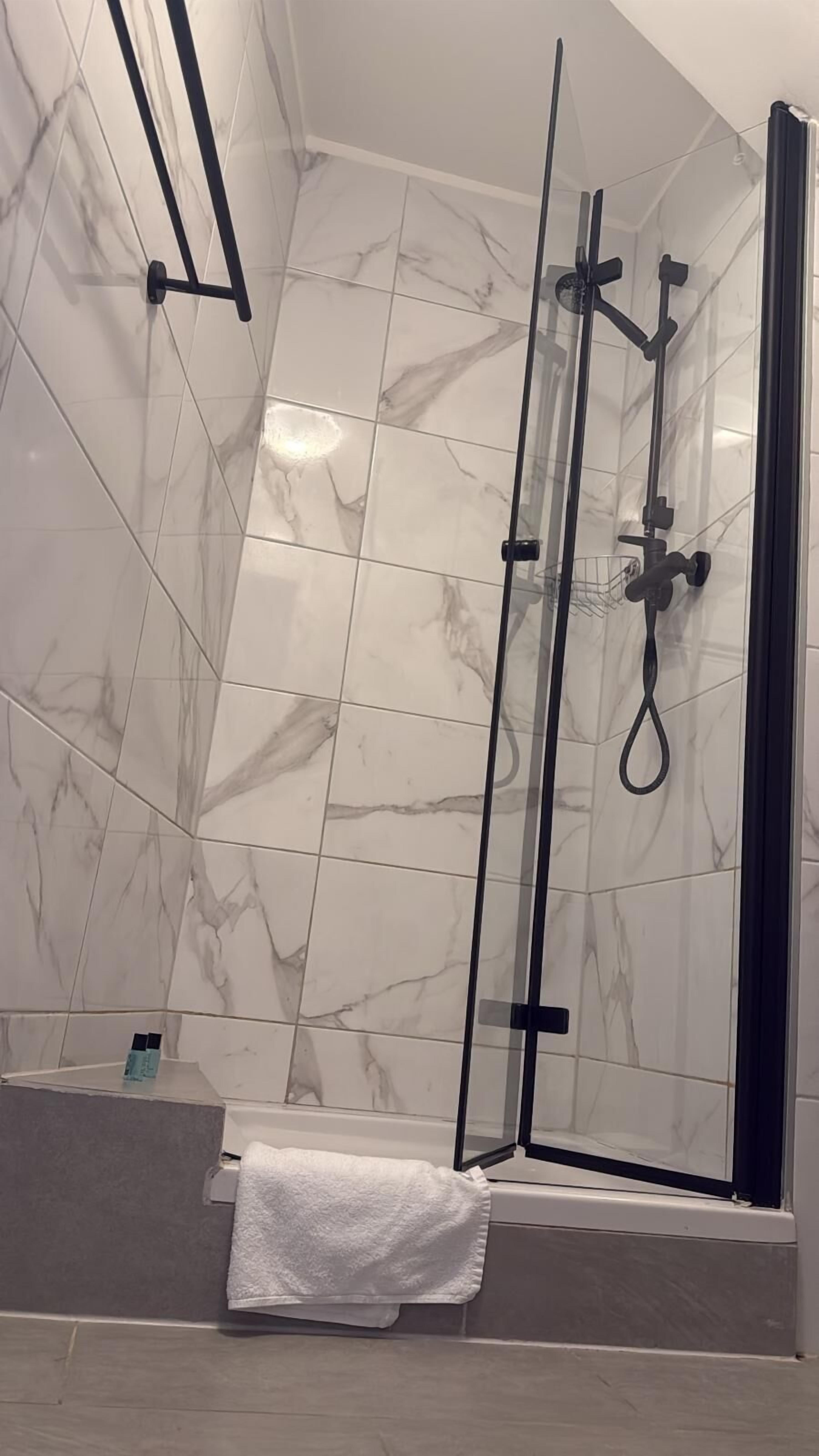 A modern bathroom with a glass-enclosed shower, marble tiles, and a white towel on the floor.