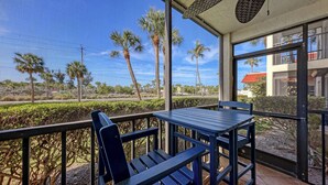 A balcony with a table and chairs, overlooking palm trees and a road. - Siesta Key - steps to the beach & pool#108 (Sarasota)
