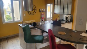 A modern kitchen with a central island, a clock on the wall, and a view of the outside through large windows. - Villa near town center (approx. 600 m) with land (Dinan)