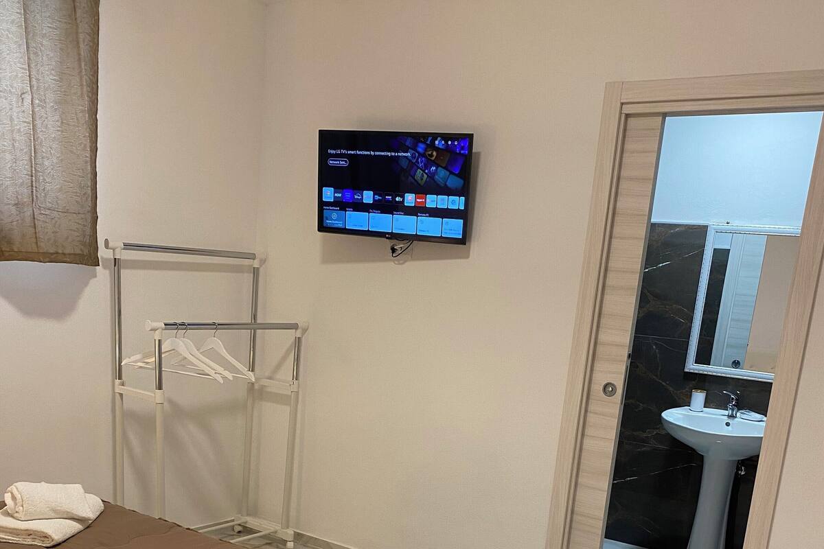 A hotel room with a bed, a TV mounted on the wall, a towel rack, and a bathroom visible through an open door.