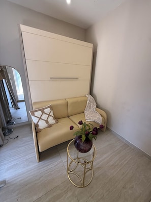 A room with a beige sofa, a round gold-framed table with a vase of flowers, and a large mirror on the wall. - STUDIO swimming pool (Bouc-Bel-Air)