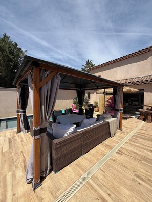A covered outdoor seating area with a pergola, wicker furniture, and a pool in the background. - STUDIO swimming pool (Bouc-Bel-Air)