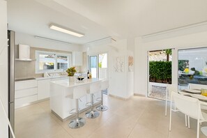 A modern kitchen with a central island, white cabinetry, and a dining area with a table and chairs. - Seaside Sunrise - 1 min walk to Green Bay (Paralimni)
