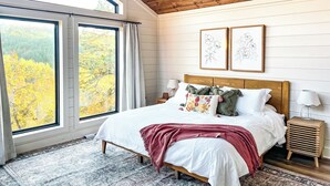 Une chambre avec une grande fenêtre, un plafond en bois et un lit agrémenté de plusieurs oreillers et d’une couverture.