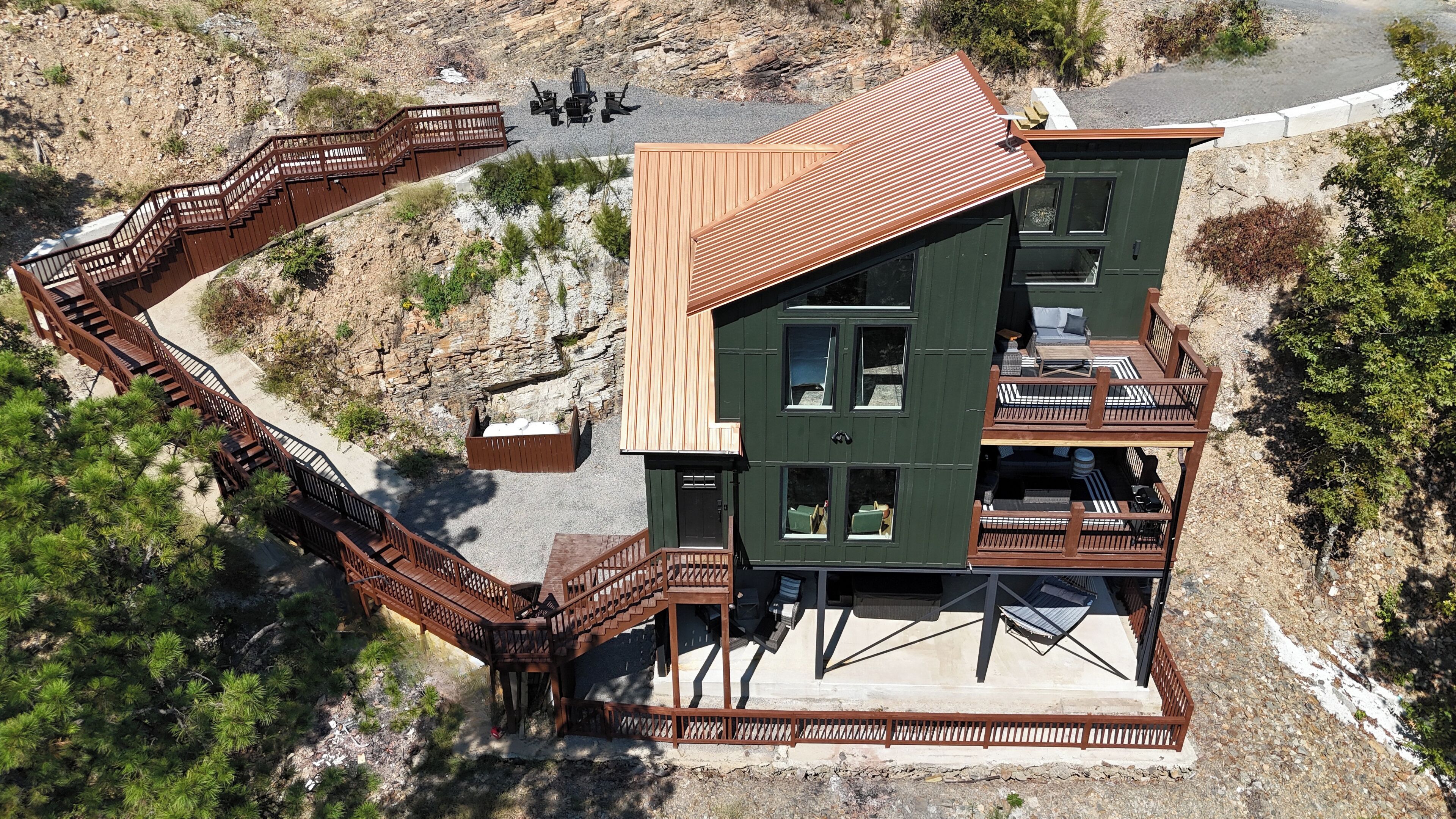 A two-story building with a wooden deck and staircase, surrounded by natural landscape.