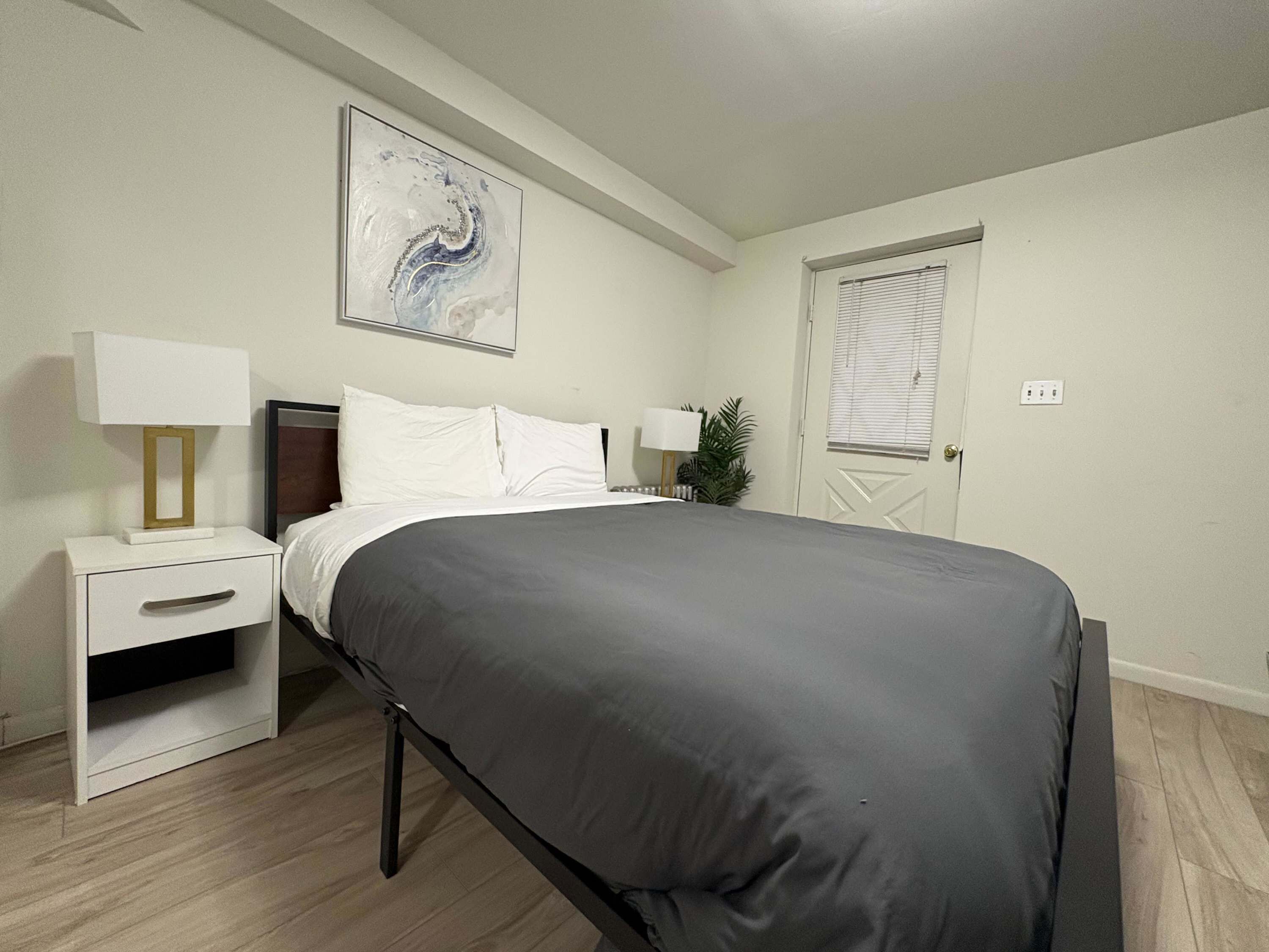 Een netjes ingerichte slaapkamer met een bed, nachtkastjes, een lamp en een schilderij aan de muur.