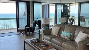 Ein geräumiges Wohnzimmer mit einer großen Couch, einem Couchtisch und Meerblick durch große Fenster.