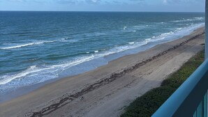 Blick auf den Strand mit Wellen, blauem Himmel und einem Balkongeländer.