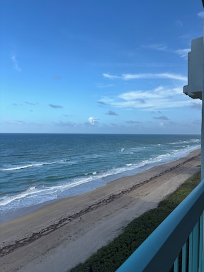 Vista de la playa con olas, cielo despejado y barandilla de balcón.