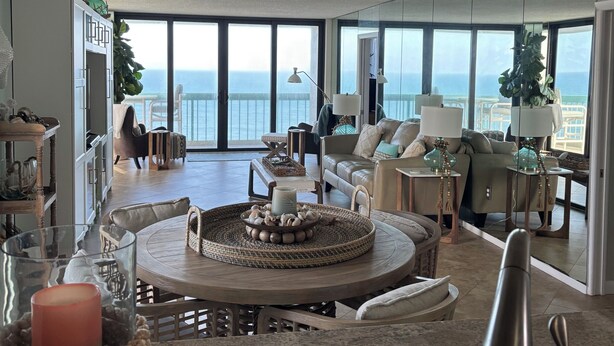 Ein geräumiger Wohnbereich mit großem Fenster zum Meer, einem Deckenventilator und einem Esstisch mit Mittelstück.