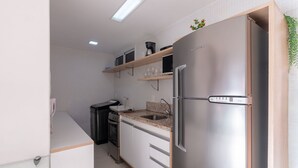 Eine kompakte Küche mit einem Edelstahlkühlschrank, einer Kaffeemaschine und einer Mikrowelle auf einer Holzablage.