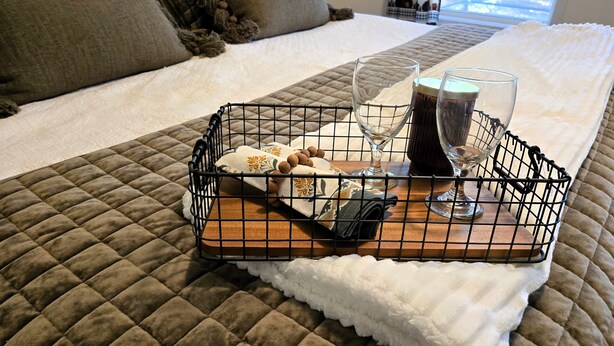 A neatly made bed with a quilted brown bedspread, a white fluffy blanket, and a tray with a bottle, glasses, and a folded towel. - Adventure-Ready St. Germain Getaway Near Lakes, Trails & Rentals (Saint Germain)
