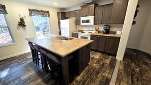 A modern kitchen with dark wood cabinets, a granite countertop, stainless steel appliances, and a large island with bar stools. - Adventure-Ready St. Germain Getaway Near Lakes, Trails & Rentals (Saint Germain)