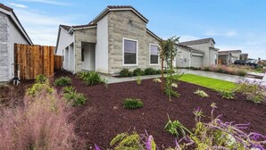 A modern residential building with a stone facade, a wooden fence, and a well-maintained garden with various plants and a lawn. - Private Bakersfield Getaway Near Downtown & Parks! (Bakersfield)