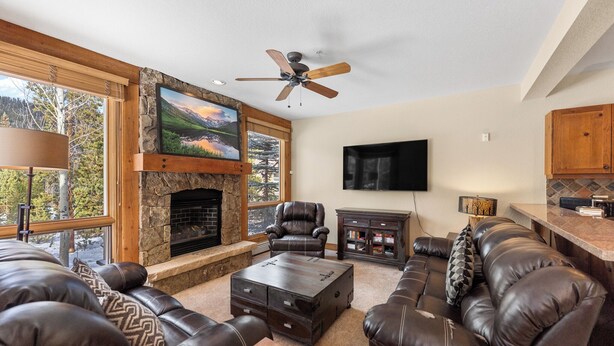 A living room with leather sofas, a stone fireplace, a ceiling fan, and a TV mounted on the wall. - Sc6522-2 (Keystone)