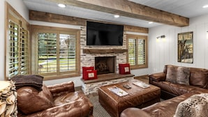 A living room with a stone fireplace, leather sofas, and a mounted TV. - Creekside Retreat in the Heart of Sun Valley! (Sun Valley)