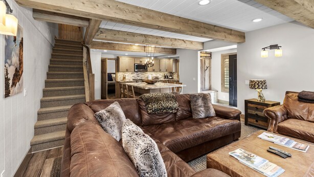A spacious living area with a brown leather sofa, a coffee table with magazines, and a staircase leading to a kitchen. - Creekside Retreat in the Heart of Sun Valley! (Sun Valley)