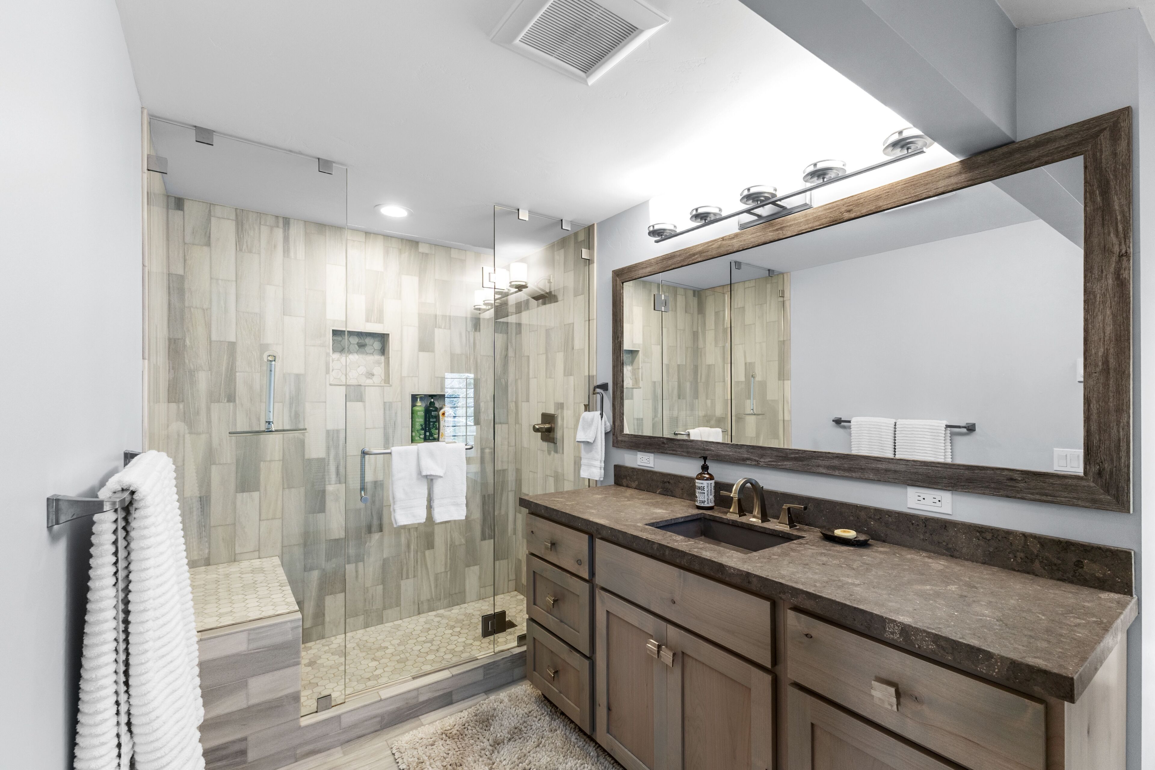 A modern bathroom with a glass shower enclosure, a large mirror, and a granite countertop.