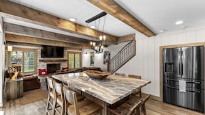 A kitchen with a marble island, wooden chairs, a stainless steel refrigerator, and a stone fireplace. - Creekside Retreat in the Heart of Sun Valley! (Sun Valley)