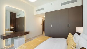 A modern hotel room with a large bed, a wardrobe, a vanity with a mirror, and a bedside table. - Vogue | Jeewar By Badr JVC near Circle Mall (Dubai)