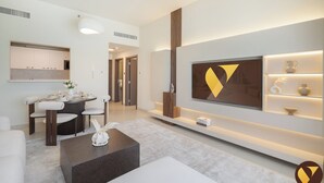 A modern living room with a dining area, a large TV mounted on the wall, and a bookshelf with decorative items. - Vogue | Jeewar By Badr JVC near Circle Mall (Dubai)