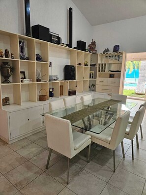 A dining area with a glass-top table and white chairs, surrounded by shelves with various decorative items. - Gorgeous 7-bedroom villa with AC in vibrant Cancún (Cancún)
