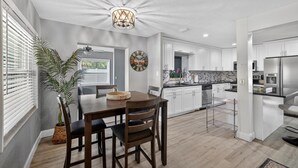 A modern kitchen with white cabinets, a stainless steel refrigerator, and a dining area with a wooden table and chairs. - 3-Bedroom Home Across from Busch Gardens (tampa)