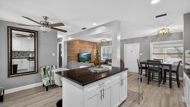 A modern kitchen with white cabinets, a black countertop, and a ceiling fan. - 3-Bedroom Home Across from Busch Gardens (tampa)