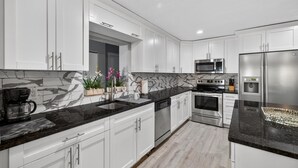 A modern kitchen with white cabinets, black countertops, a built-in microwave, stainless steel appliances, and a marble backsplash. - 3-Bedroom Home Across from Busch Gardens (tampa)