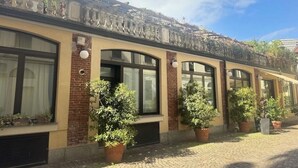 A building with a brick facade, large windows, and potted plants along the walkway. - A Casa di Imma - Elegant studio apartment in Porta Rom (Milano)