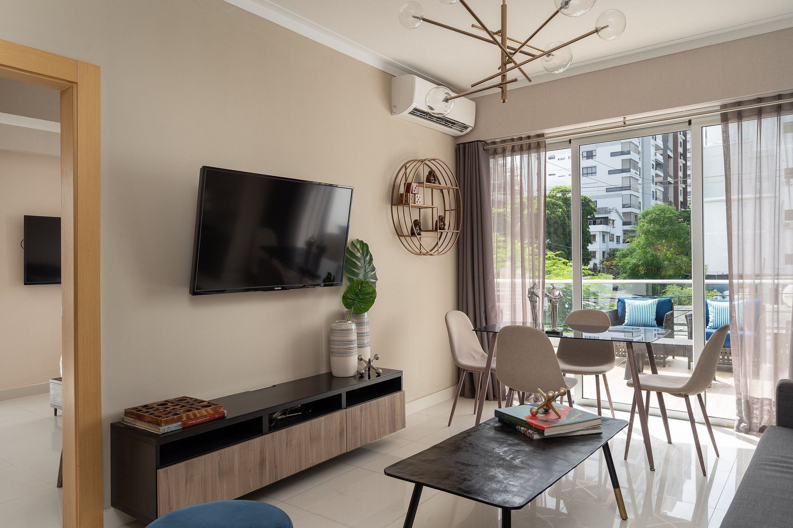 Ein modernes Wohnzimmer mit Flachbildfernseher, einer Holzkonsole, einem Esstisch mit Stühlen und Blick auf den Balkon.