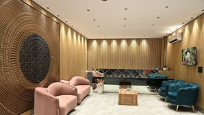 Eine moderne Lobby mit geschwungenen Wänden, einer Sitzecke mit rosa und türkisfarbenen Stühlen, einem Marmorboden und einem Kamin.