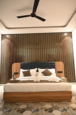 A neatly made bed with a wooden headboard, a ceiling fan, and a wall with vertical wooden slats. - Troy Resorts and Wellness (Zirakpur)