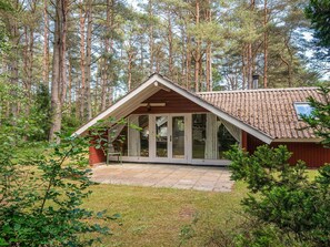 En stuga med ett sluttande tak, stora glasdörrar och en stenbelagd uteplats.