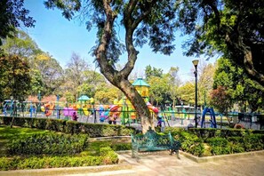 A park with playground equipment, a large tree, and a bench. - Suite Morada • Moderna y Céntrica hasta 7 viajeros (Mexico City)