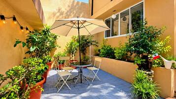 An outdoor patio with a round table and chairs, surrounded by potted plants and a flag.