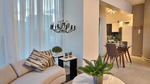 Una sala de estar moderna con sofá, una araña y un comedor con mesa y sillas.