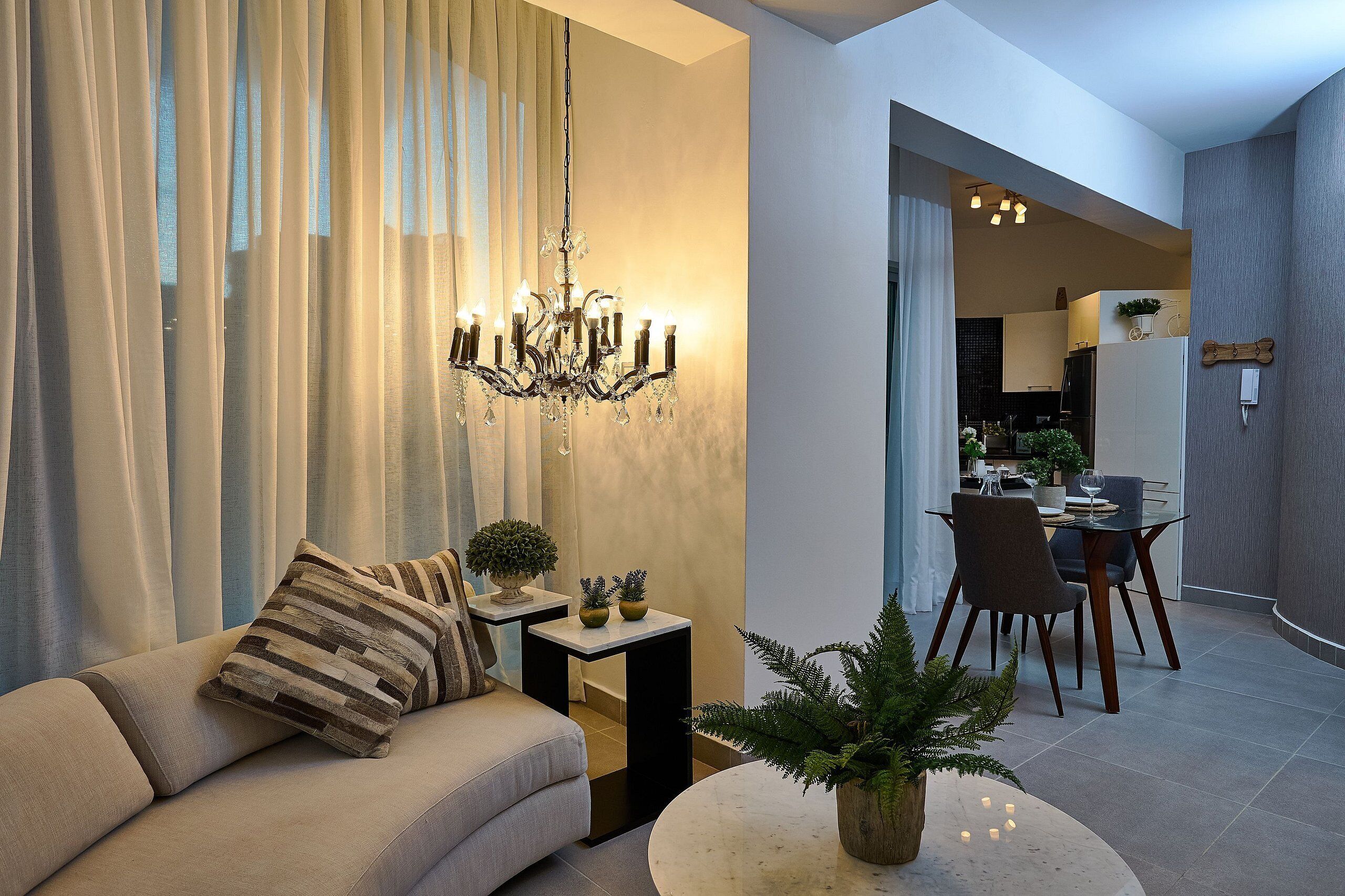 A modern living room with a sofa, a chandelier, a dining area with chairs and a table, and a potted plant.