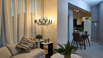 A modern living room with a sofa, a chandelier, a dining area with chairs and a table, and a potted plant.