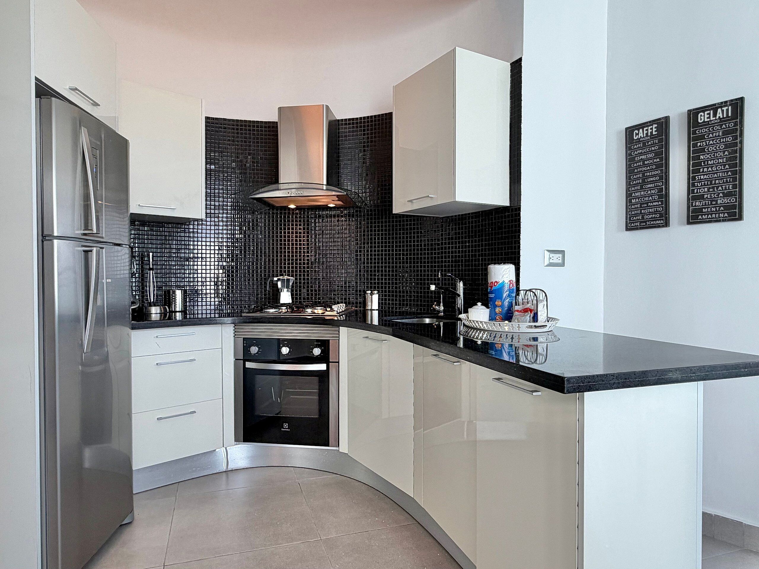 A modern kitchen with a stainless steel refrigerator, a built-in oven, and a black tiled backsplash.