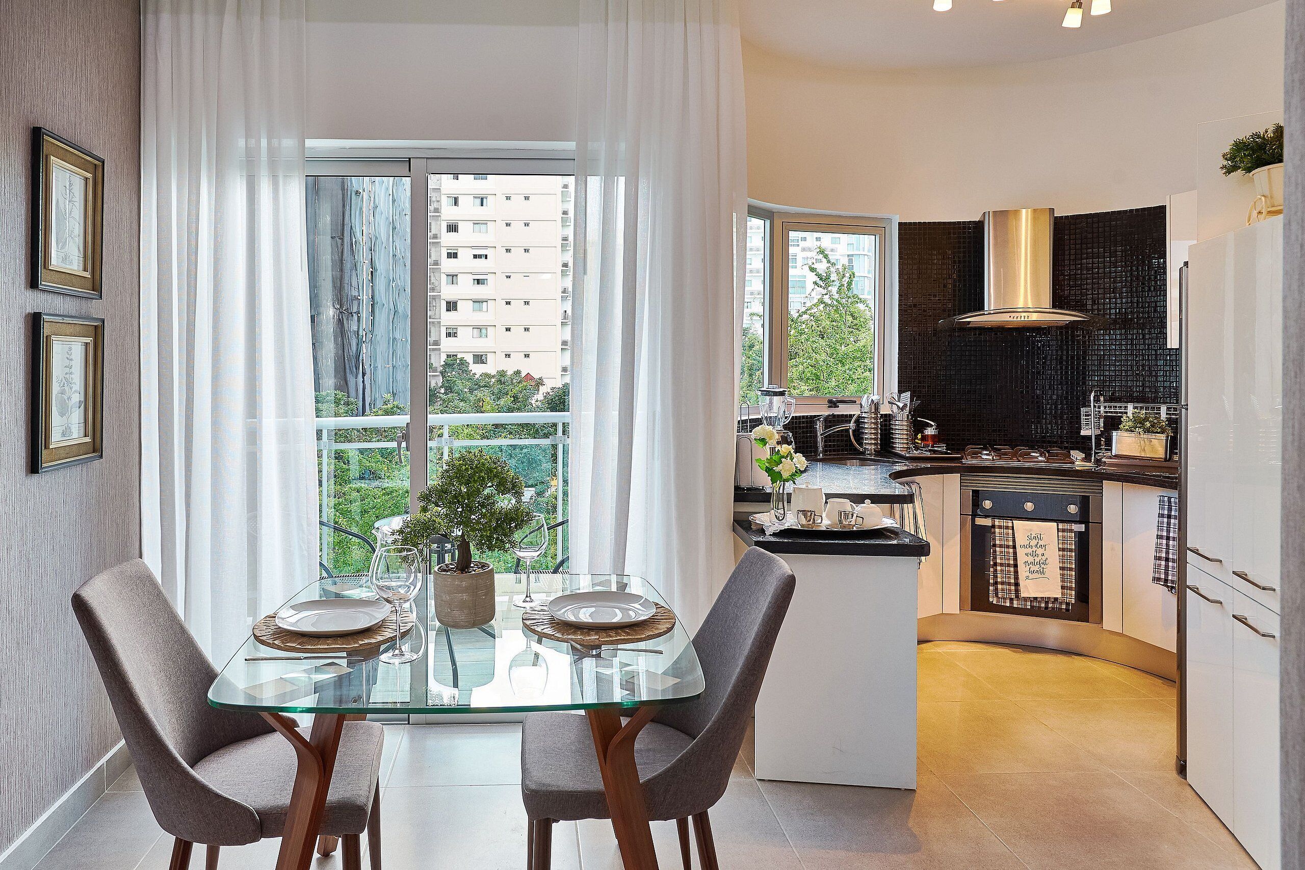 A modern kitchen with a glass dining table, two chairs, and a view of a cityscape through large windows.