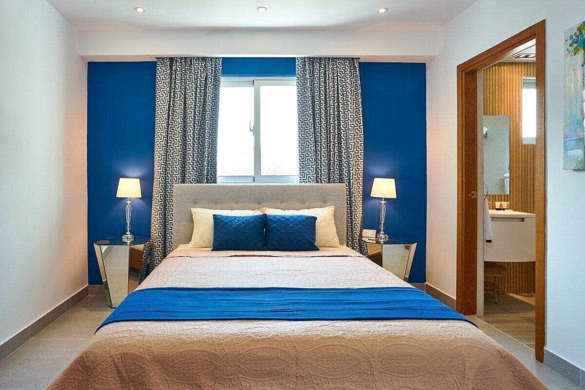 A modern hotel room with a large bed, blue curtains, and a view of the bathroom.