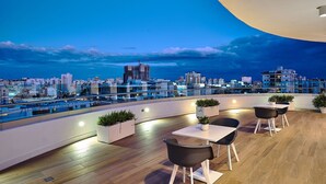 Una terraza en la azotea con vista a la ciudad, suelo de madera y mobiliario exterior moderno.