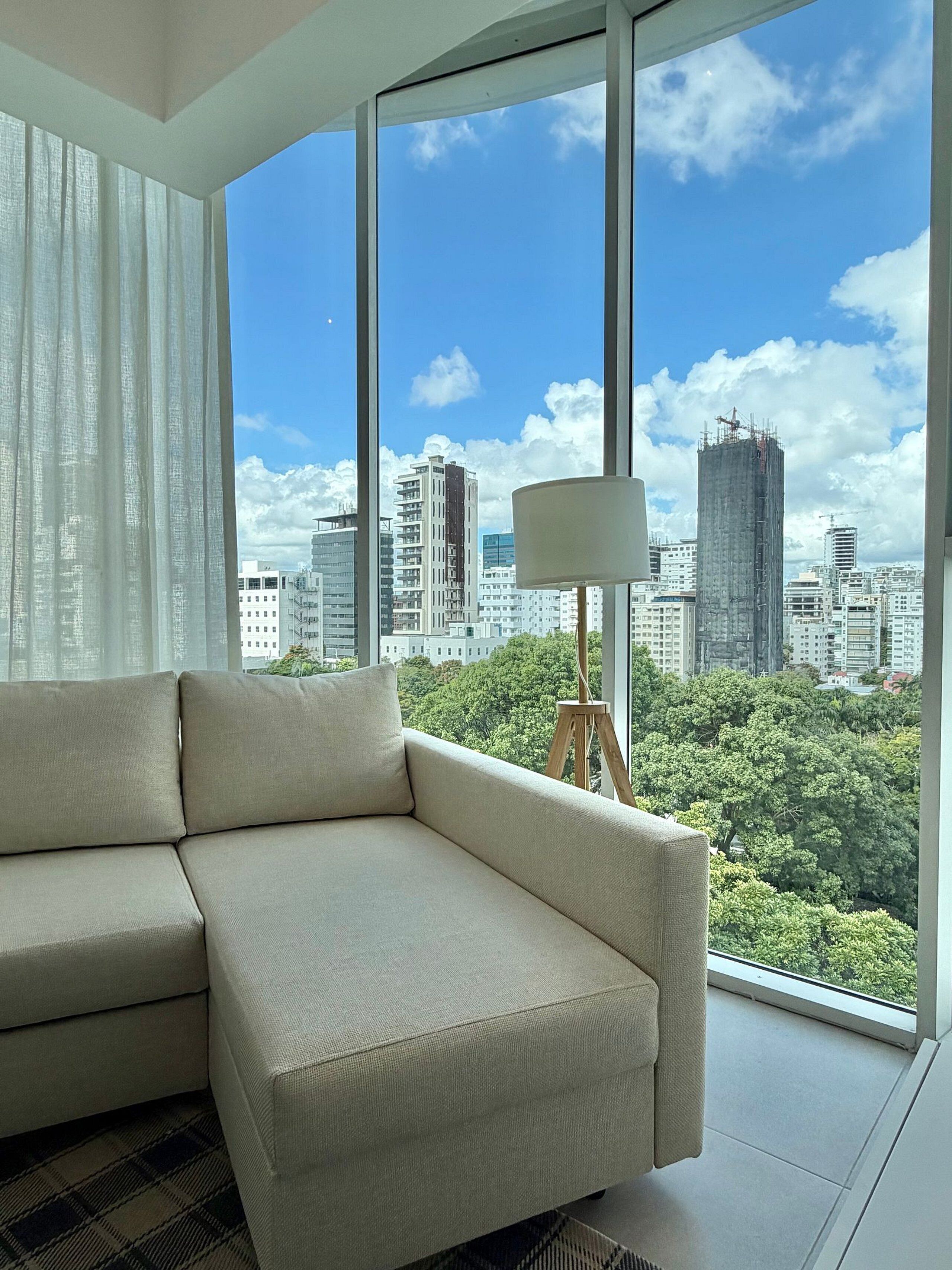 Un salón moderno con un ventanal grande, un sofá, una lámpara y vistas a la ciudad.